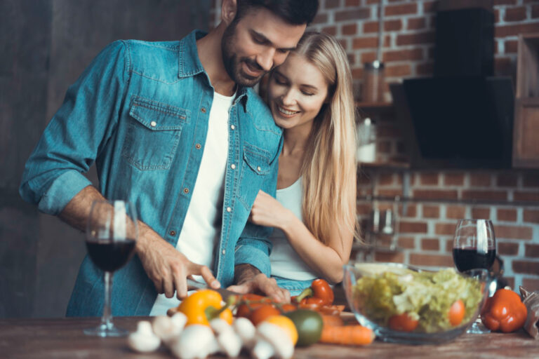 Šťastný pár sa smeje pri spoločnom varení večere v kuchyni pri svetle sviečok počas Valentína.